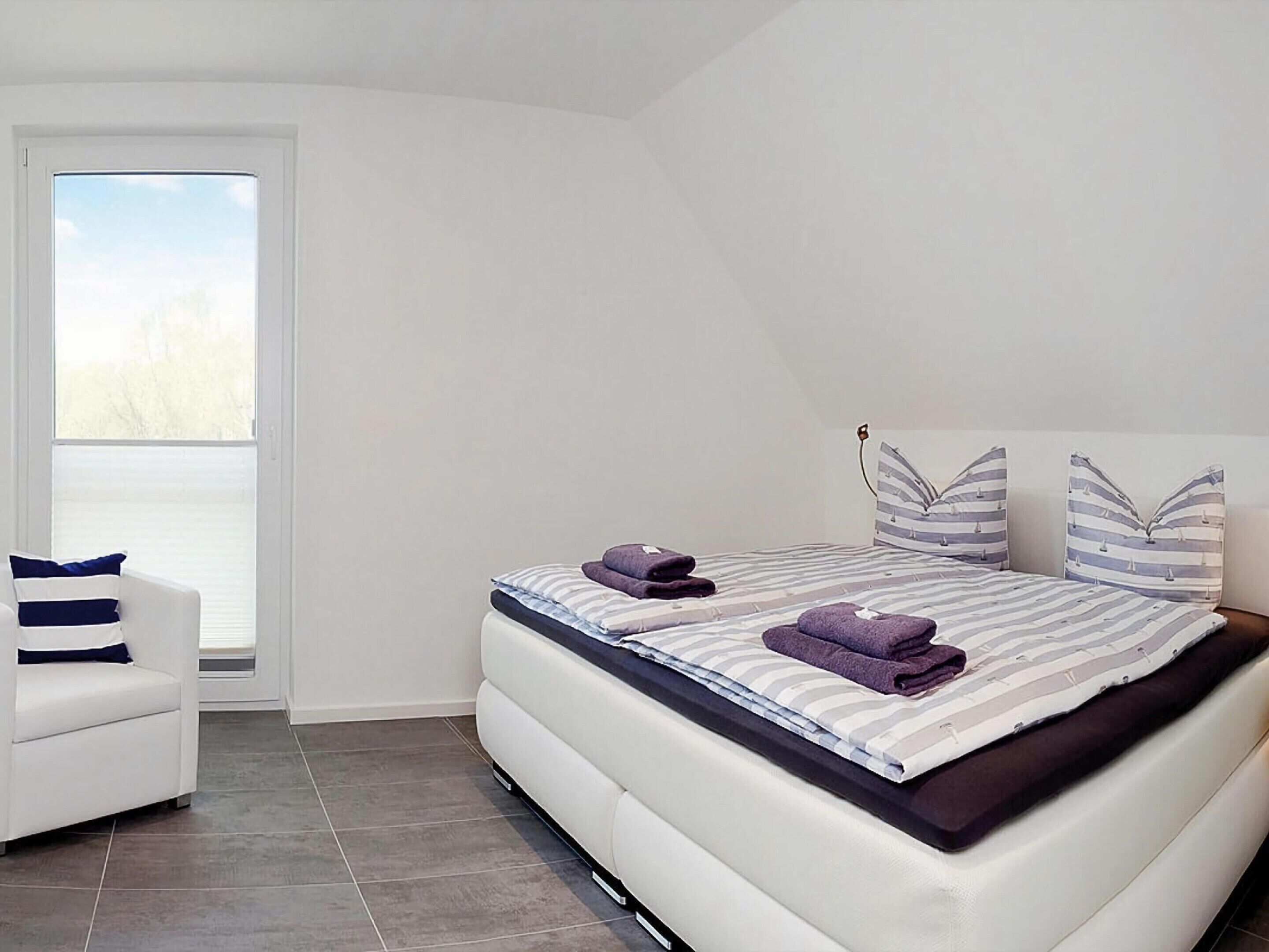 Un dormitorio moderno con cama, una silla y un ventanal grande.