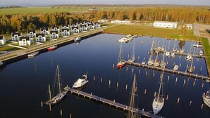 A marina with multiple docks and boats, surrounded by a row of white buildings with dark roofs, likely residential or commercial structures. - Modern Eingerichtetes Ferienhaus auf Usedom (Peenemünde)