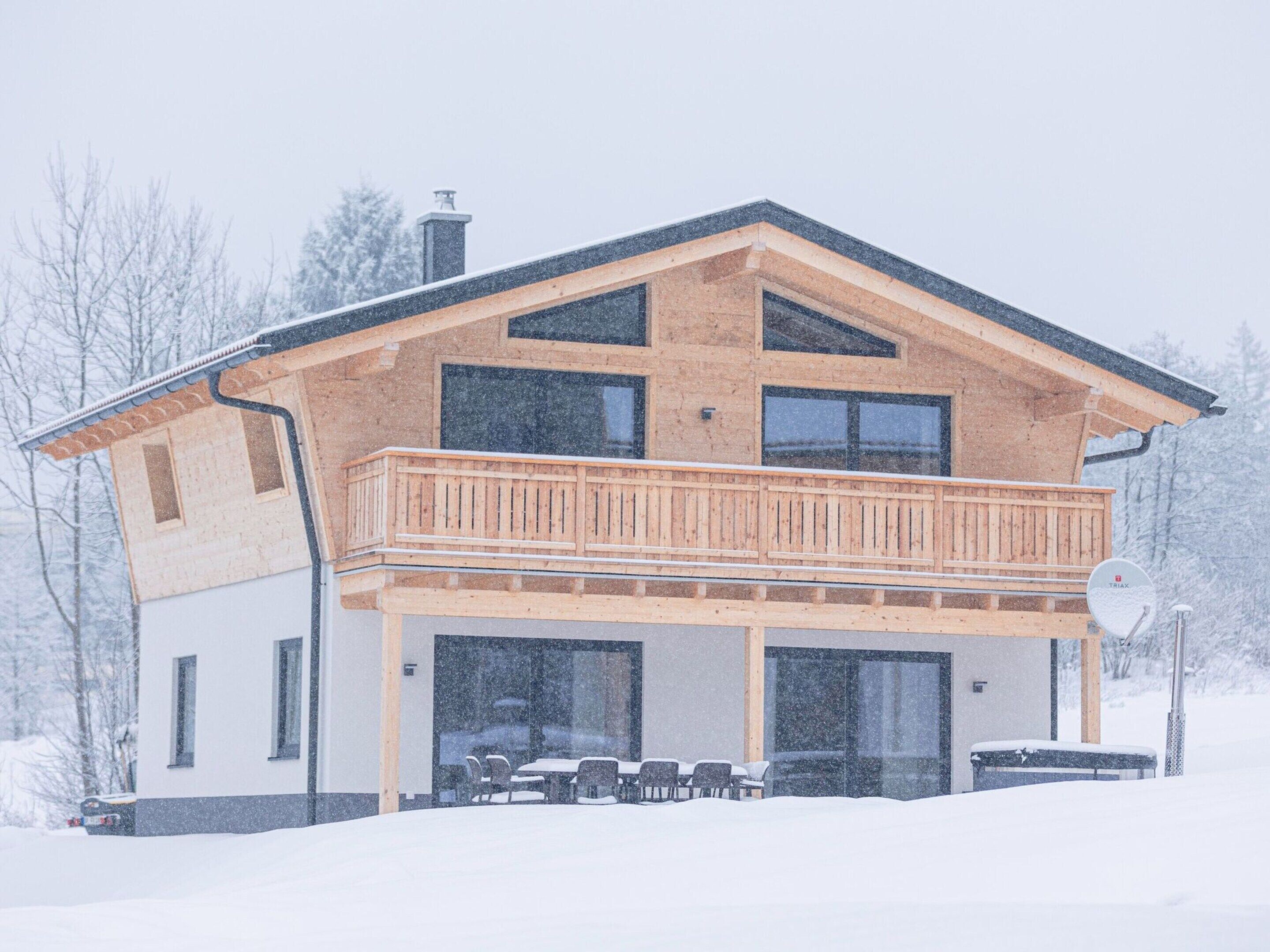 A two-story house with a balcony, large windows, and a covered outdoor seating area.