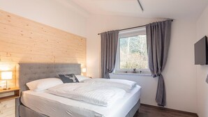 A bedroom with a large bed, wooden headboard, a window with curtains, a bedside lamp, and a flat-screen TV mounted on the wall. - Chalet Arber in St.englmar With its own Hottube (Sankt Englmar)