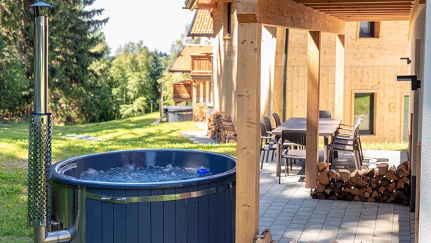 A wooden cabin with a hot tub, outdoor seating, and a stack of firewood. - Chalet Arber in St.englmar With its own Hottube (Sankt Englmar)