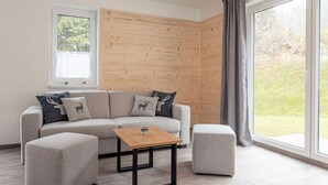 A modern living room with a sectional sofa, two ottomans, a wooden coffee table, and a large window with curtains. - Chalet Arber in St.englmar With its own Hottube (Sankt Englmar)