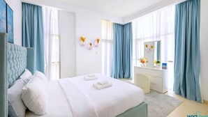 Habitación de hotel moderna con una cama grande, un escritorio y una silla. Hay cortinas en las ventanas y un pequeño jarrón con flores en la pared.