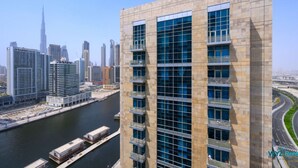 Un edificio moderno de gran altura con varios balcones, ubicado cerca de una masa de agua con un puerto deportivo al frente.
