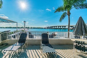 A deck with lounge chairs and umbrellas overlooking a body of water with a bridge in the distance.
