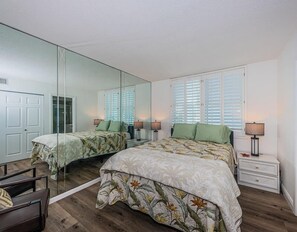 A bedroom with two beds, a large mirror, and a nightstand with a lamp.