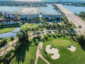 Un campo de golf con una gran masa de agua, un puente y un hotel de varios pisos.