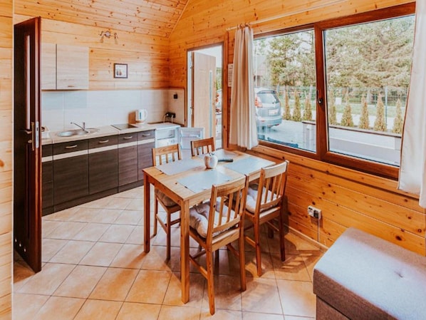 A wooden cabin with a kitchen, dining area, and large windows.