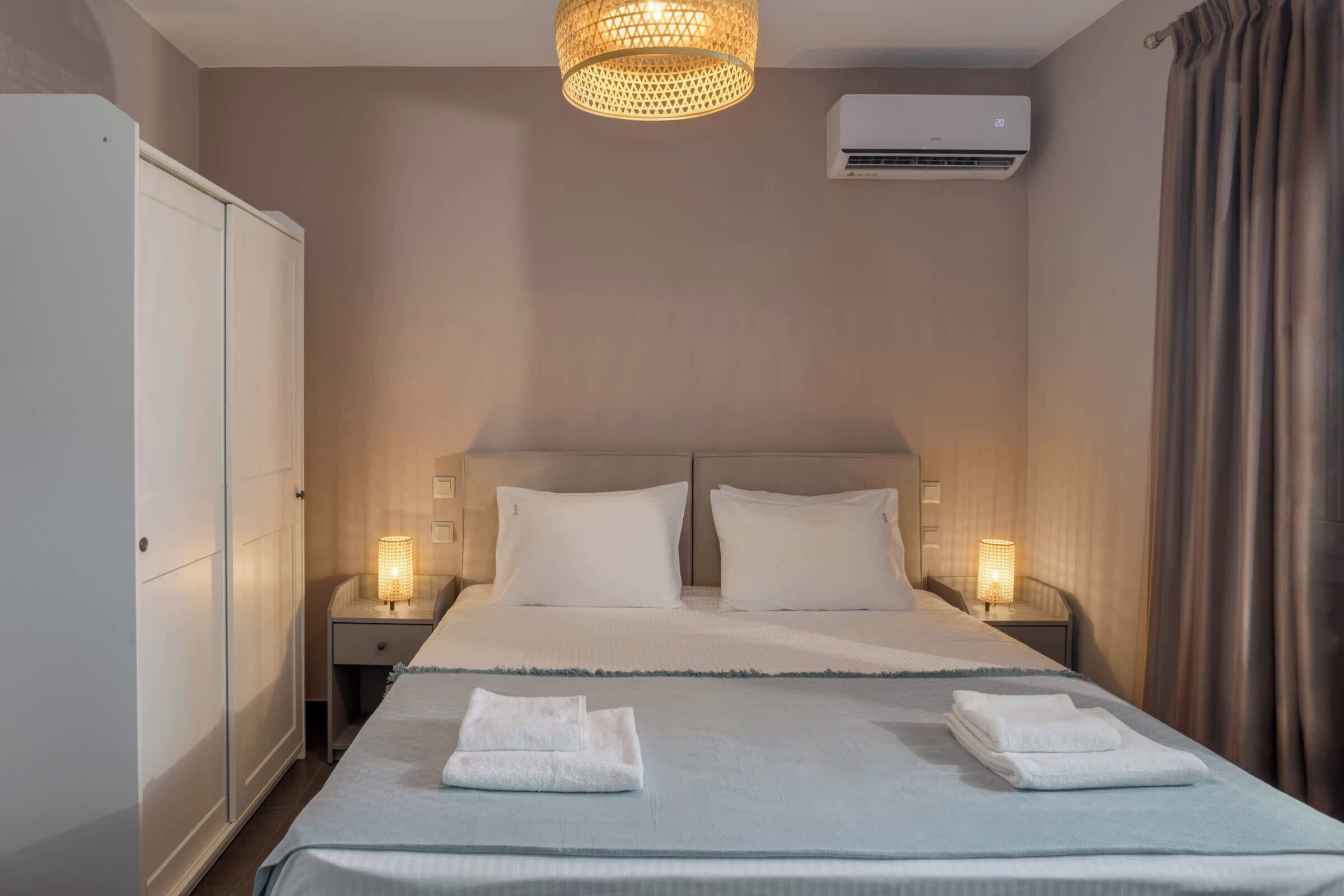A hotel room with a large bed, two bedside lamps, an air conditioning unit, and a wardrobe.