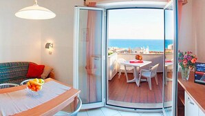 A room with a dining table, a sofa, and a glass door leading to a balcony with a view of the sea. - Holiday Flat in Pretty Residence With Communal Pool in Pietra Ligure (Pietra Ligure)