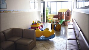 A living room with a brown sofa, a yellow and blue ride-on toy, and a wooden playhouse. - Holiday Flat in Pretty Residence With Communal Pool in Pietra Ligure (Pietra Ligure)