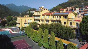 Un hôtel à plusieurs étages doté de balcons, d’un court de tennis et surplombant un paysage montagneux.