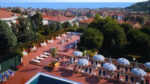 Une piscine sur le toit, avec une eau d’un bleu limpide, entourée de chaises longues et de parasols, offrant une vue sur une ville côtière.