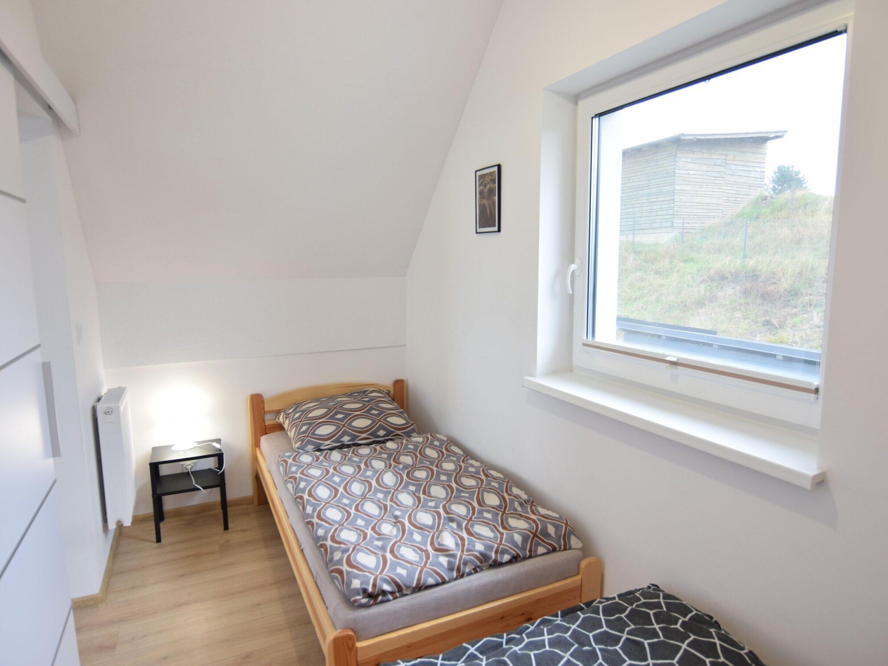 A small, single-bed room with a window, a bedside table, and a radiator.