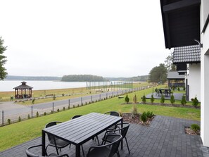 En uteplats med ett bord och stolar med utsikt över en sjö, ett lusthus och en sportplan.