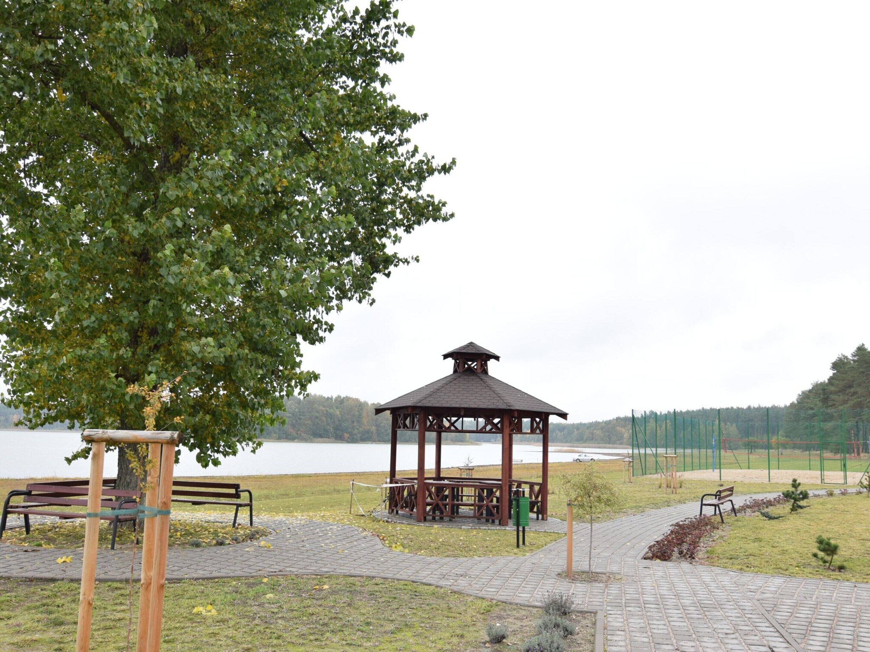 Ein Pavillon mit Vordach, Bänken und einem Picknicktisch in einem Park mit einem See im Hintergrund.