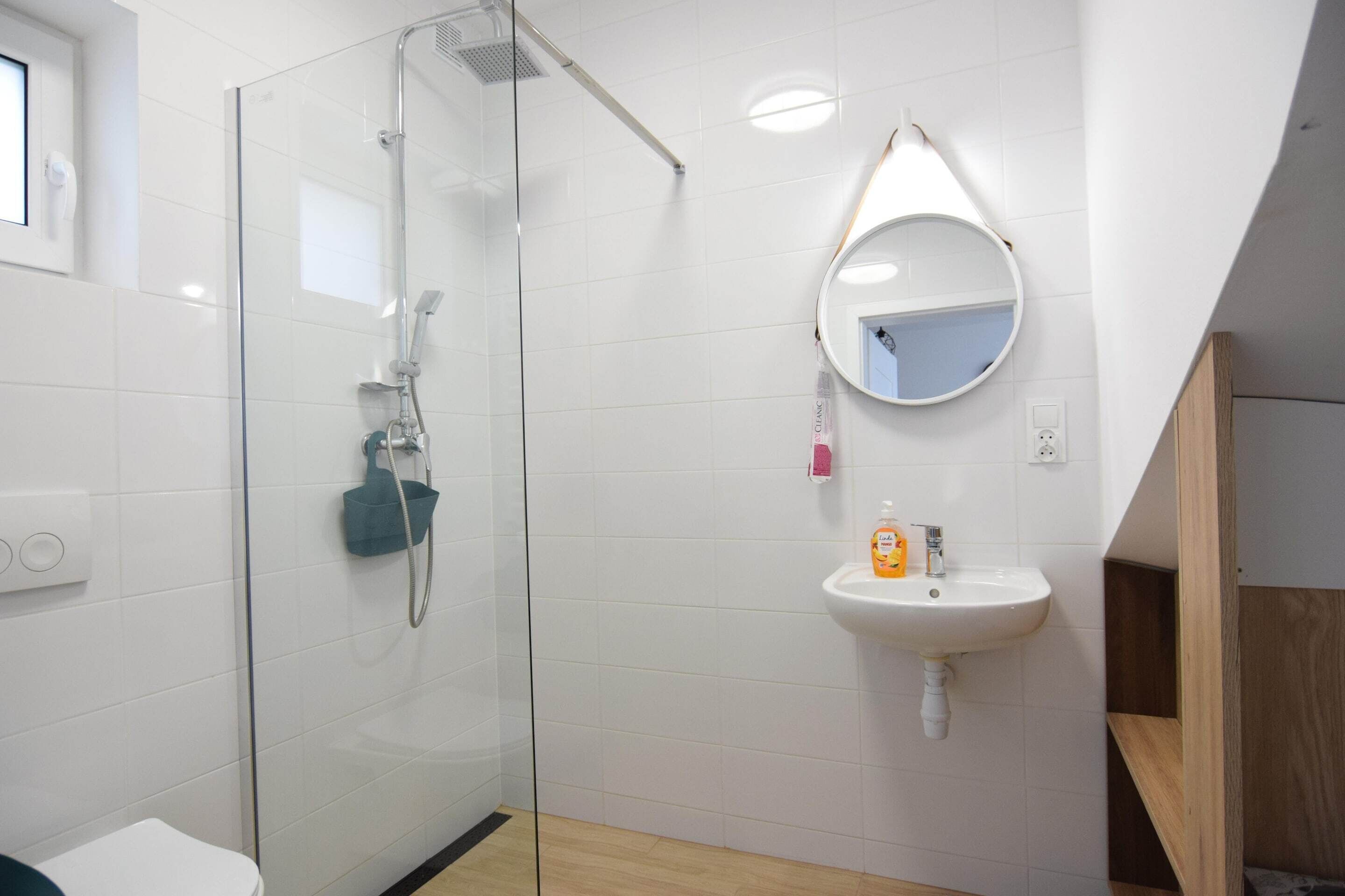 A modern bathroom with a glass-enclosed shower, a white sink with a mirror, and a wooden shelf.