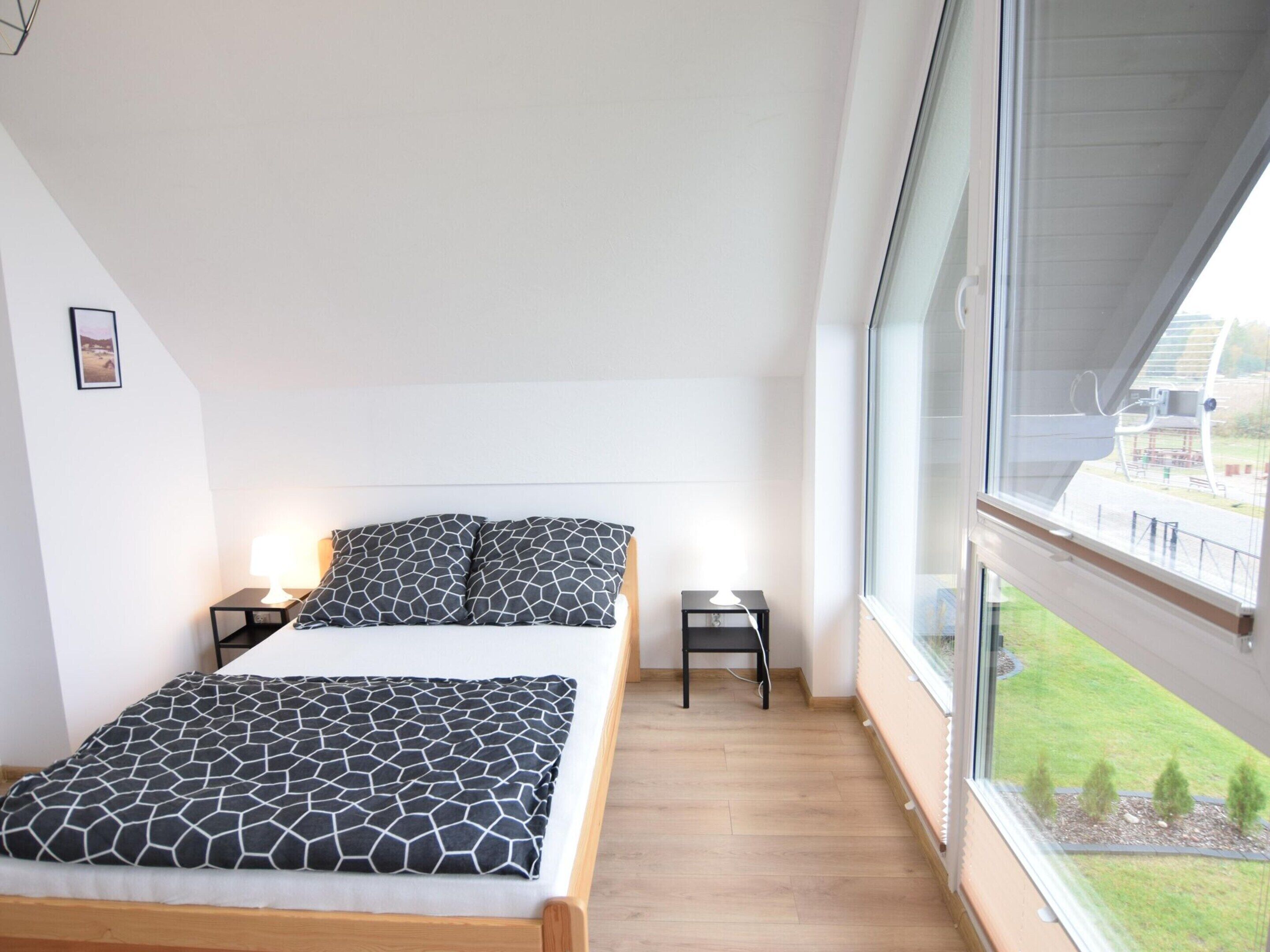 A bedroom with a bed, two bedside tables, a window with a view of a park, and a picture on the wall.