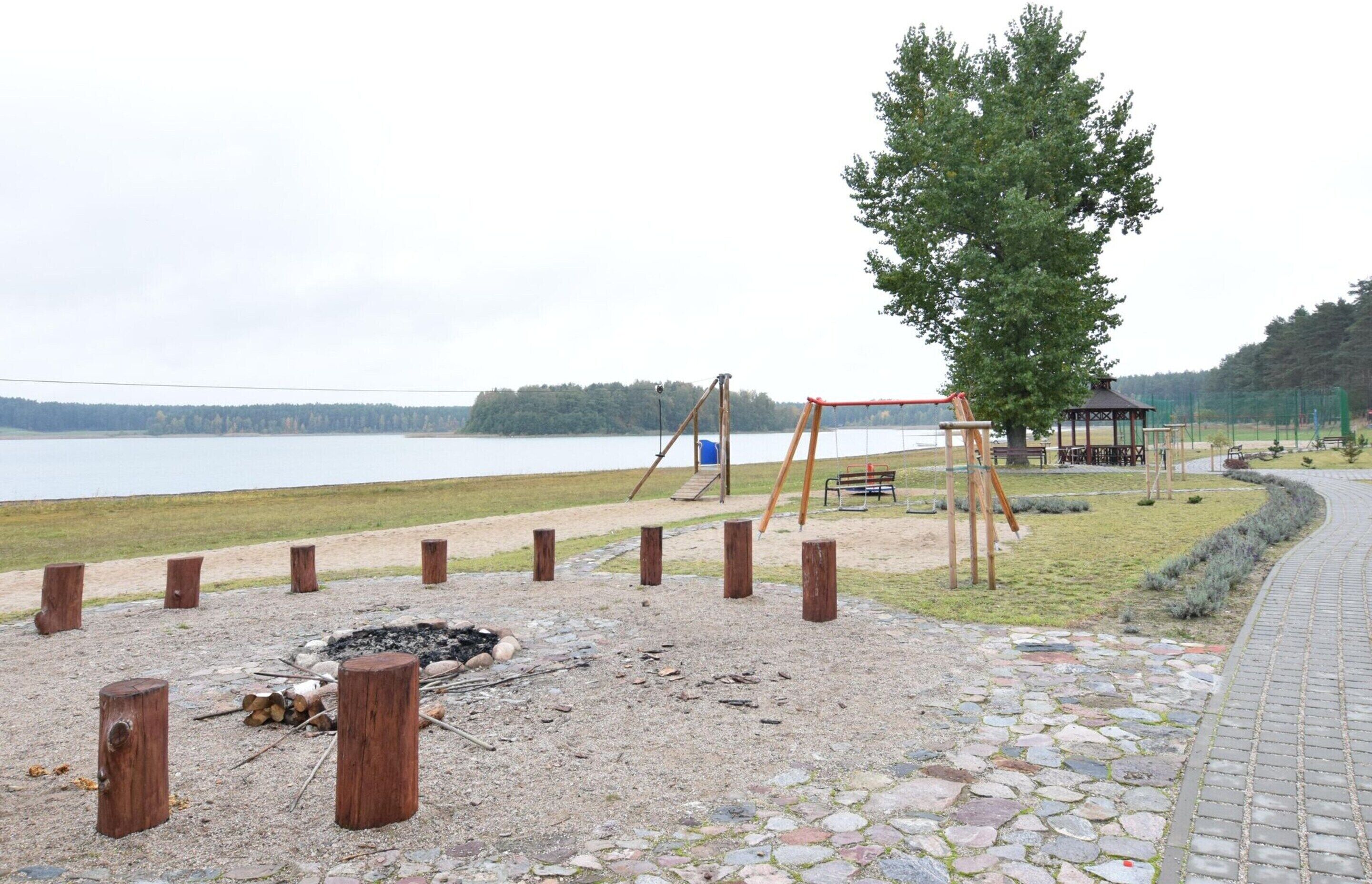 A lakeside park with a swing set, a gazebo, and a fire pit area.