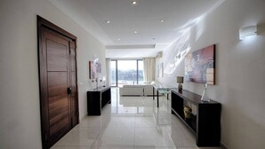A modern hotel lobby with a wooden door, a glass coffee table, and a large window offering a city view.