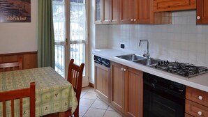 Una cocina con armarios de madera, una estufa a gas, un fregadero y una zona de comedor con mesa y sillas.