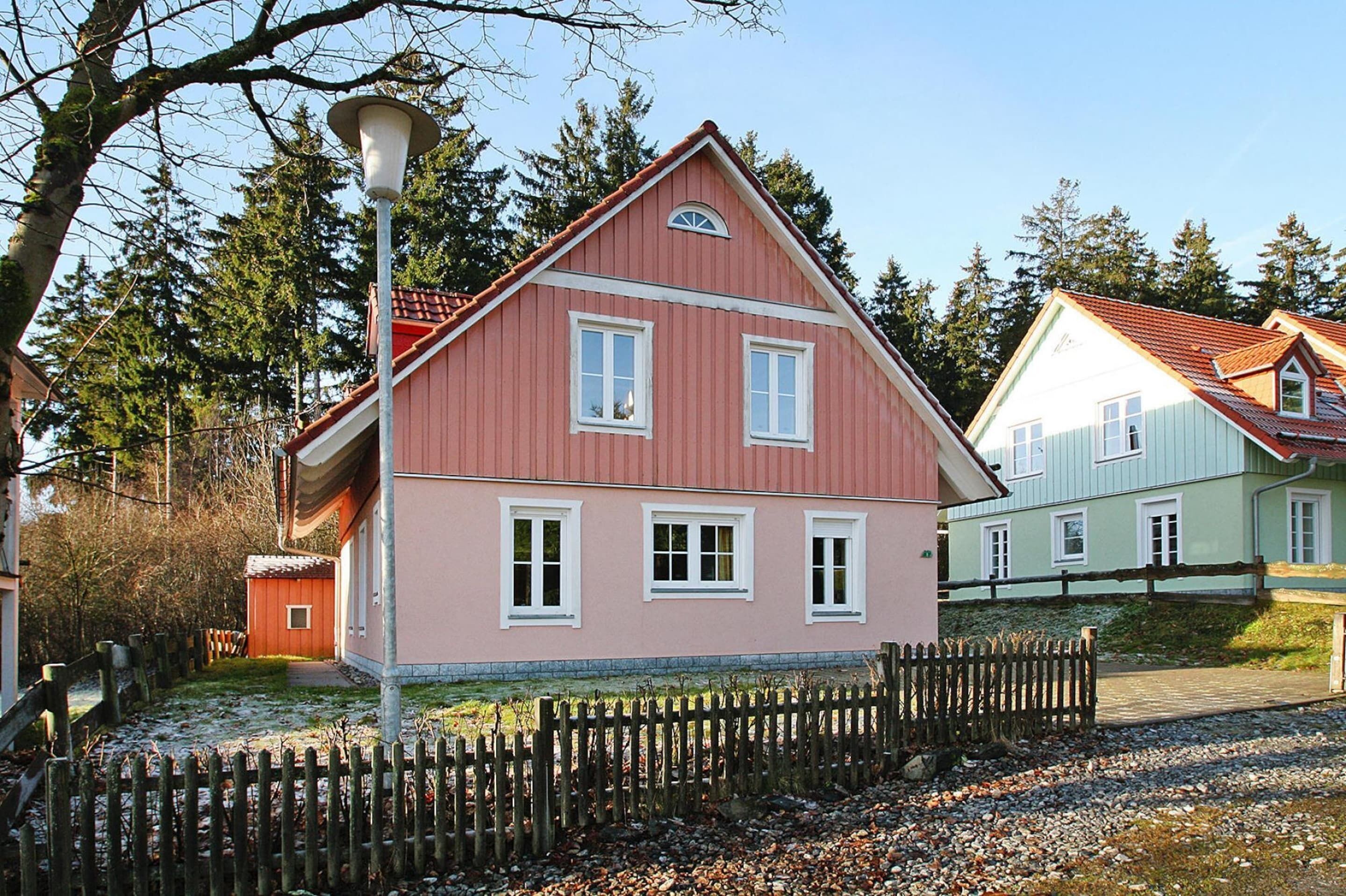 A two-story house with a red facade and white trim, a small attached shed, and a wooden fence in front.