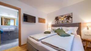 A double bed with a wooden headboard, a flat-screen TV mounted on the wall, a painting above the bed, and a bedside lamp. - Apartment in Neukirchen by Wildkogelbahn (Neukirchen am Grossvenediger)