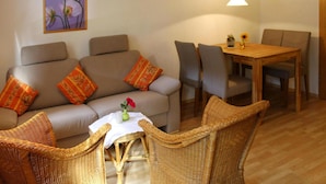 Un salon comprenant un canapé, deux fauteuils, une table à manger avec des chaises, une petite table avec un vase et un luminaire suspendu.