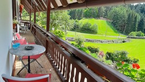 Un balcon avec une table et des chaises, donnant sur un paysage verdoyant, avec des arbres et une colline.