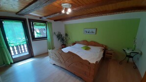 Une chambre à coucher avec un lit en bois, un mur vert, une fenêtre avec des rideaux et un ventilateur de plafond.