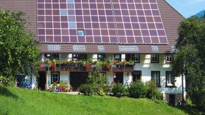 Un bâtiment doté d’un grand toit recouvert de panneaux solaires, d’une façade blanche et d’un balcon agrémenté de plantes.