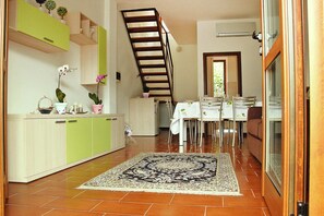 Una cocina con gabinetes verdes, un comedor con mesa y sillas, y una escalera.