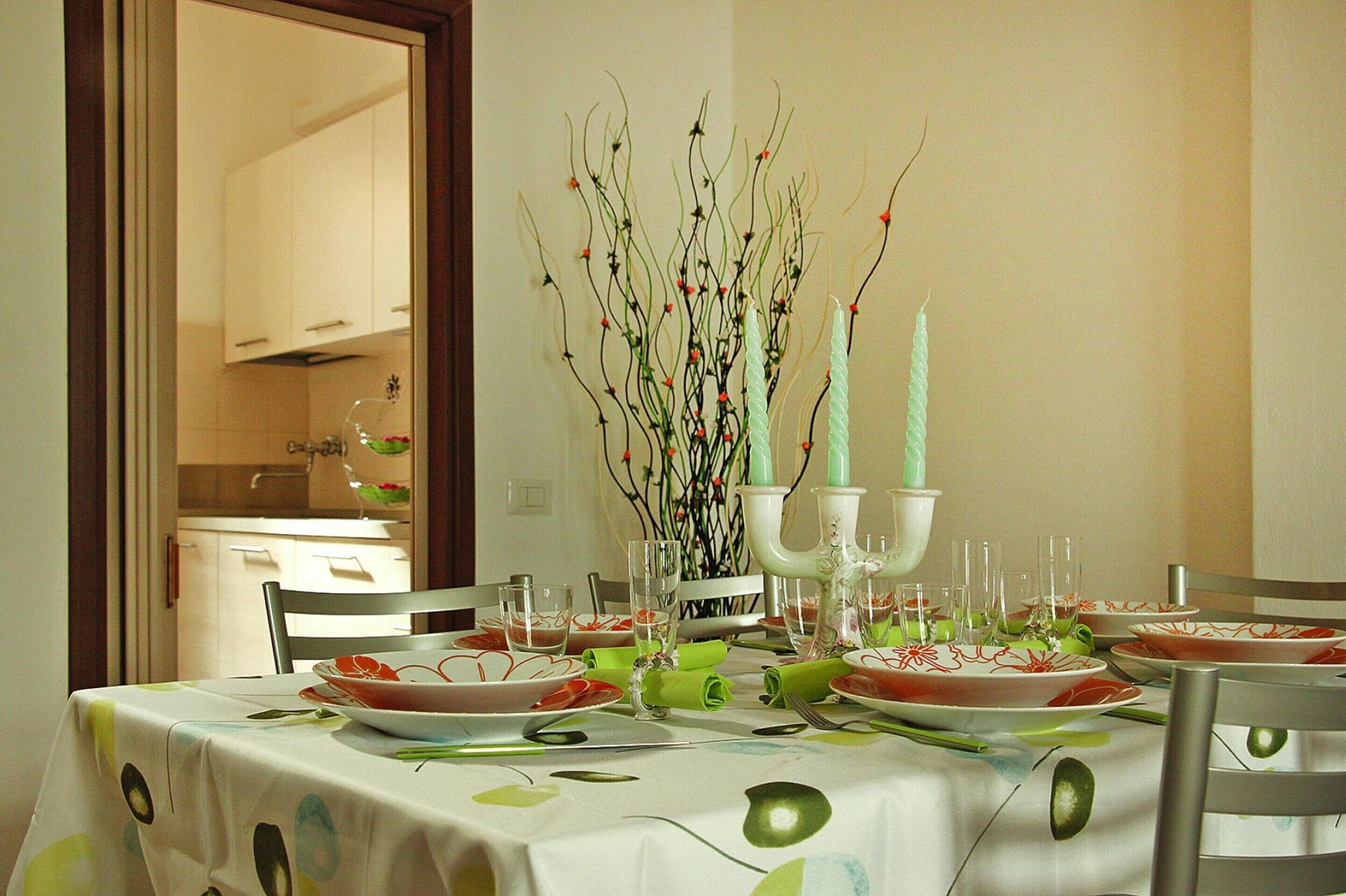 A dining table set with plates, glasses, and a centerpiece of branches with red berries.