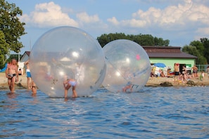 People in transparent spheres on a body of water, with a building and trees in the background. - Holiday Home in Stepnica With Sauna & Jacuzzi (Stepnica)