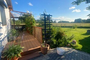 A wooden deck with potted plants, a metal trellis, and a clear view of a grassy field. - Holiday Home in Stepnica With Sauna & Jacuzzi (Stepnica)