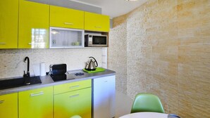 A compact kitchen with yellow cabinets, a microwave, a kettle, and a small refrigerator. There is a table with a polka dot tablecloth and a clear glass jar. - 2-room Holiday Apartment Close to the Beach (Kołobrzeg)