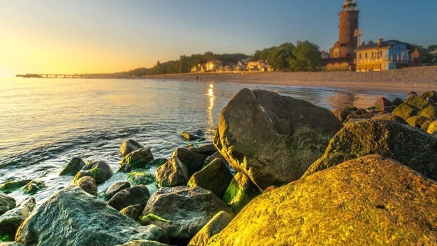 A coastal scene with a lighthouse, rocky shoreline, and buildings in the background. - 2-room Holiday Apartment Close to the Beach (Kołobrzeg)