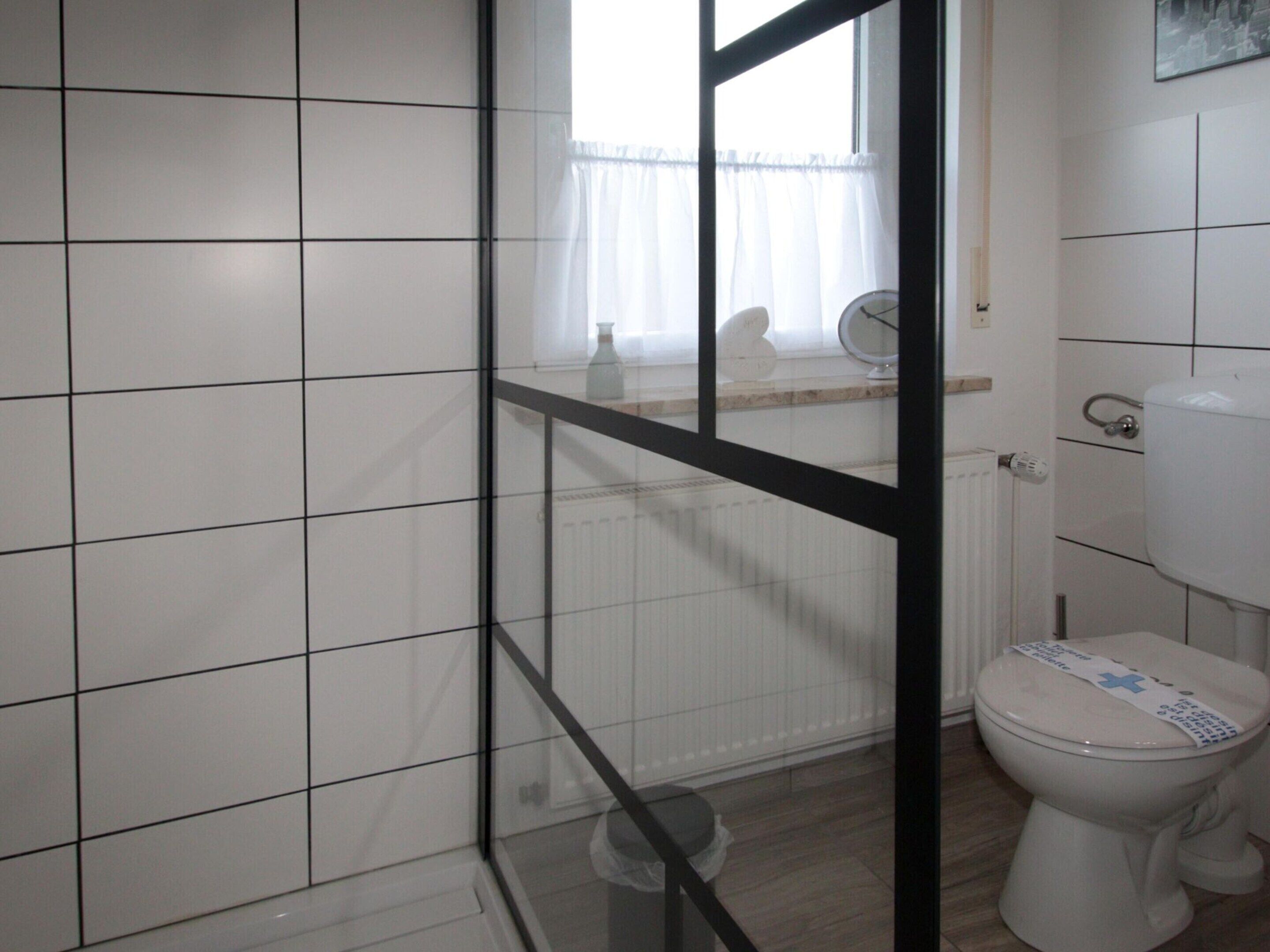 A bathroom with white tiles, a toilet, a radiator, and a window with a curtain.