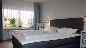 A neatly made bed with white linens, a dark headboard, and a bedside table with lamps. - Ferienwohnung Nahe Nordsee Wattwanderung (Berumbur)