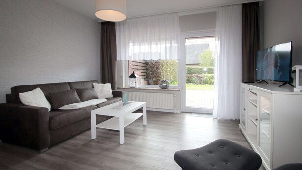 A modern living room with a sofa, coffee table, and TV. - Ferienwohnung Nahe Nordsee Wattwanderung (Berumbur)