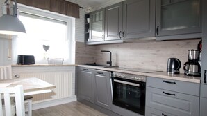 A modern kitchen with grey cabinets, a built-in oven, and a window with a heart-shaped decoration. - Ferienwohnung Nahe Nordsee Wattwanderung (Berumbur)