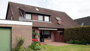 A two-story house with a brick facade, a green garage door, and a small front yard with red flowers. - Ferienwohnung Nahe Nordsee Wattwanderung (Berumbur)