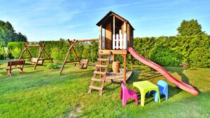 A wooden play structure with a slide, swings, and a climbing ladder in a grassy area. - Holiday Home by Lake Jamno With Pool (gmina Sianów)
