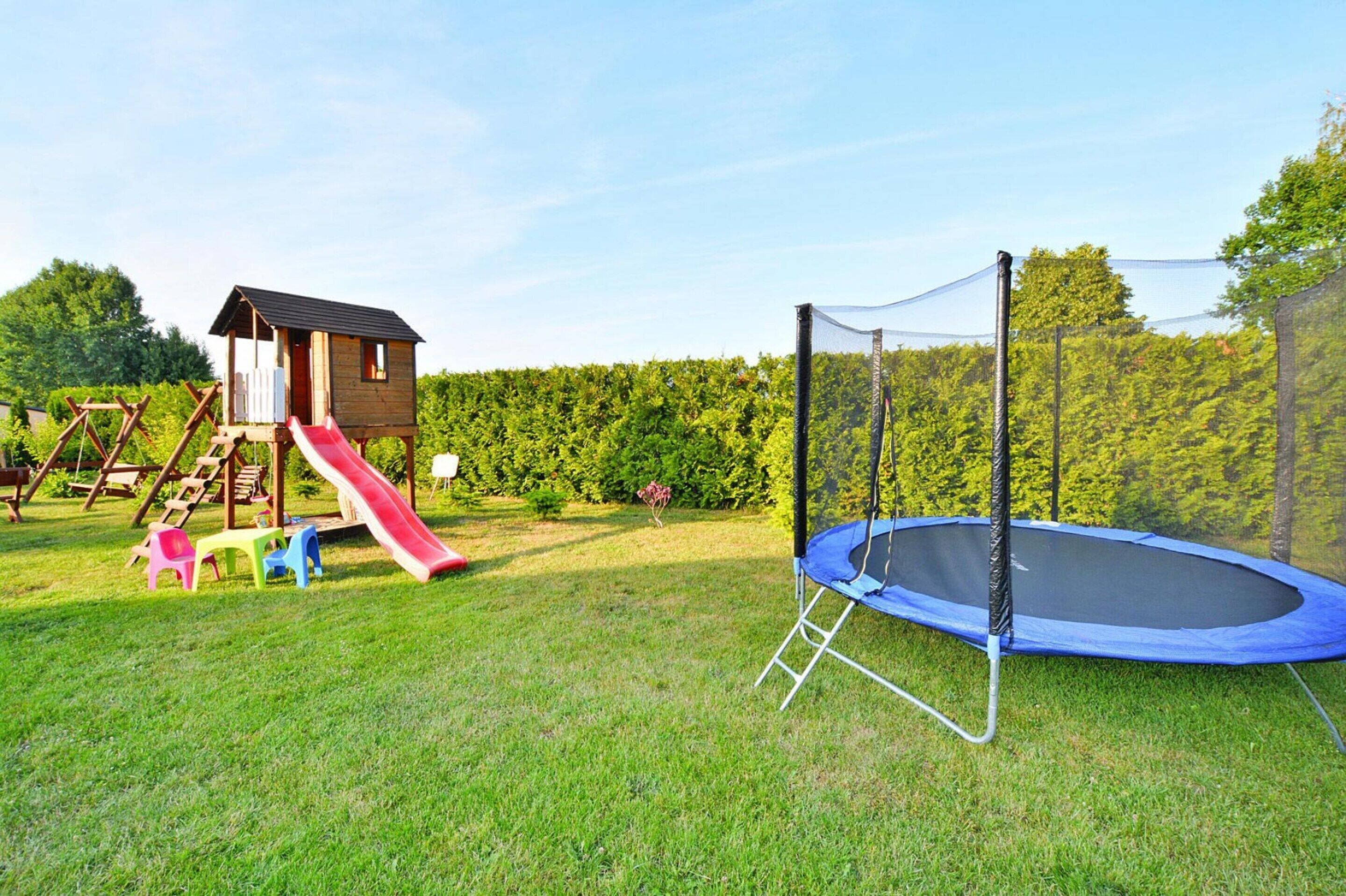 En legeplads med rutchebane, gyngestativ og trampolin i en græsplæne.