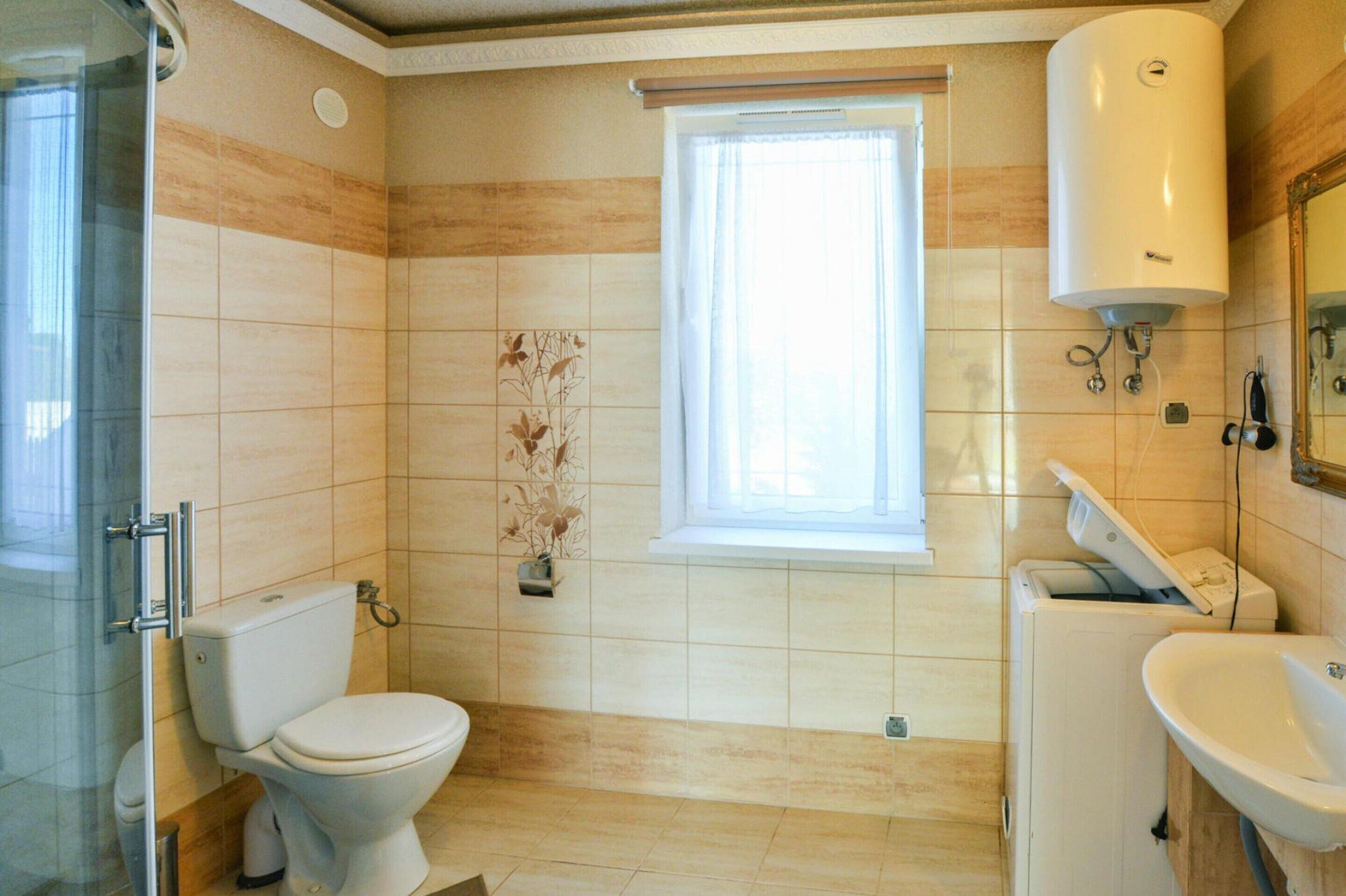 Een badkamer met een toilet, een wastafel, een raam en een douche.