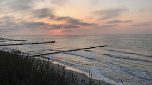A coastal scene with a sunset over the ocean, featuring a sandy beach and wooden piers extending into the water. - Holiday Home by Lake Jamno With Pool (gmina Sianów)