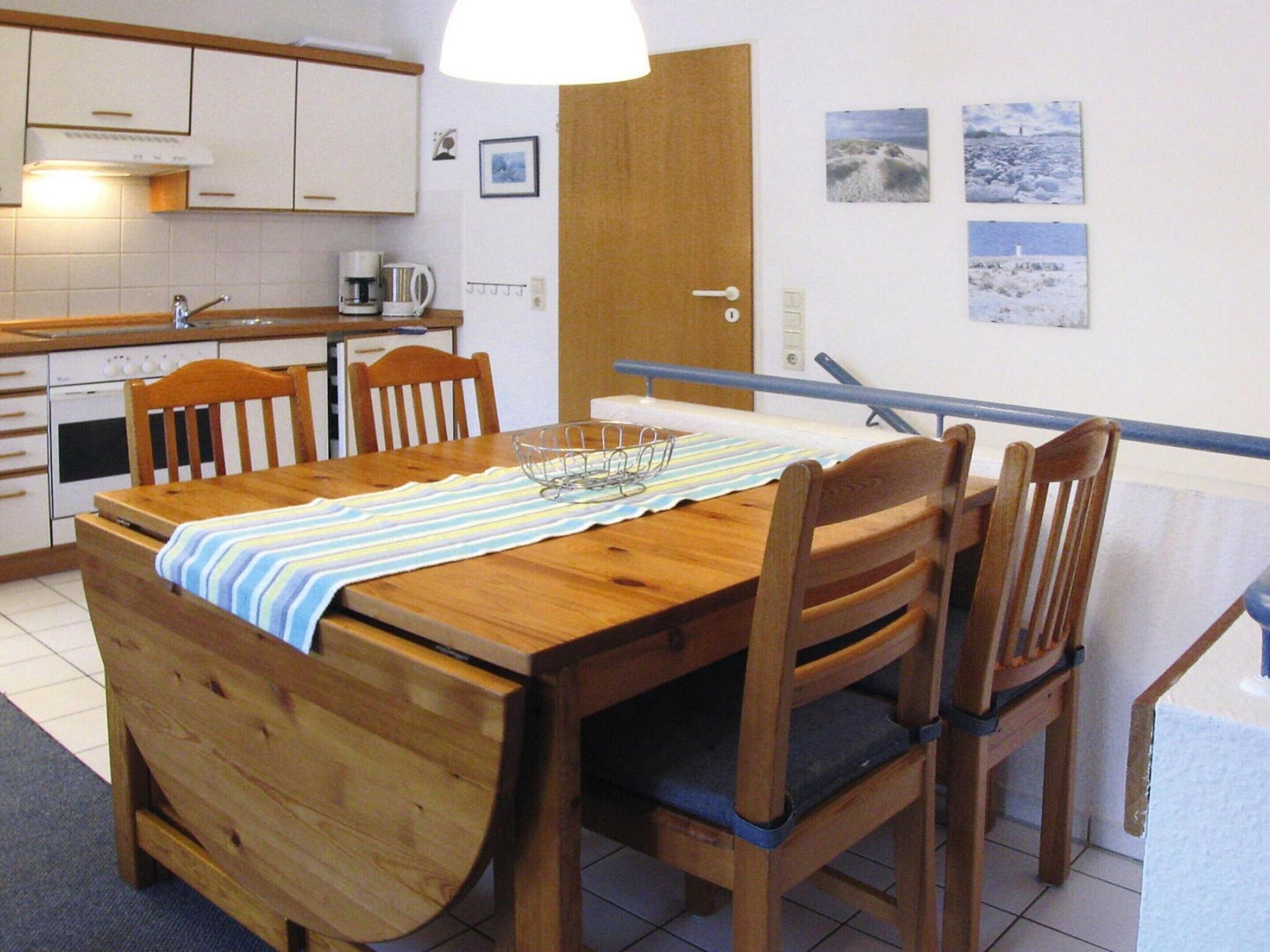 A wooden dining table with chairs, a coffee maker, and a kettle on the kitchen counter.