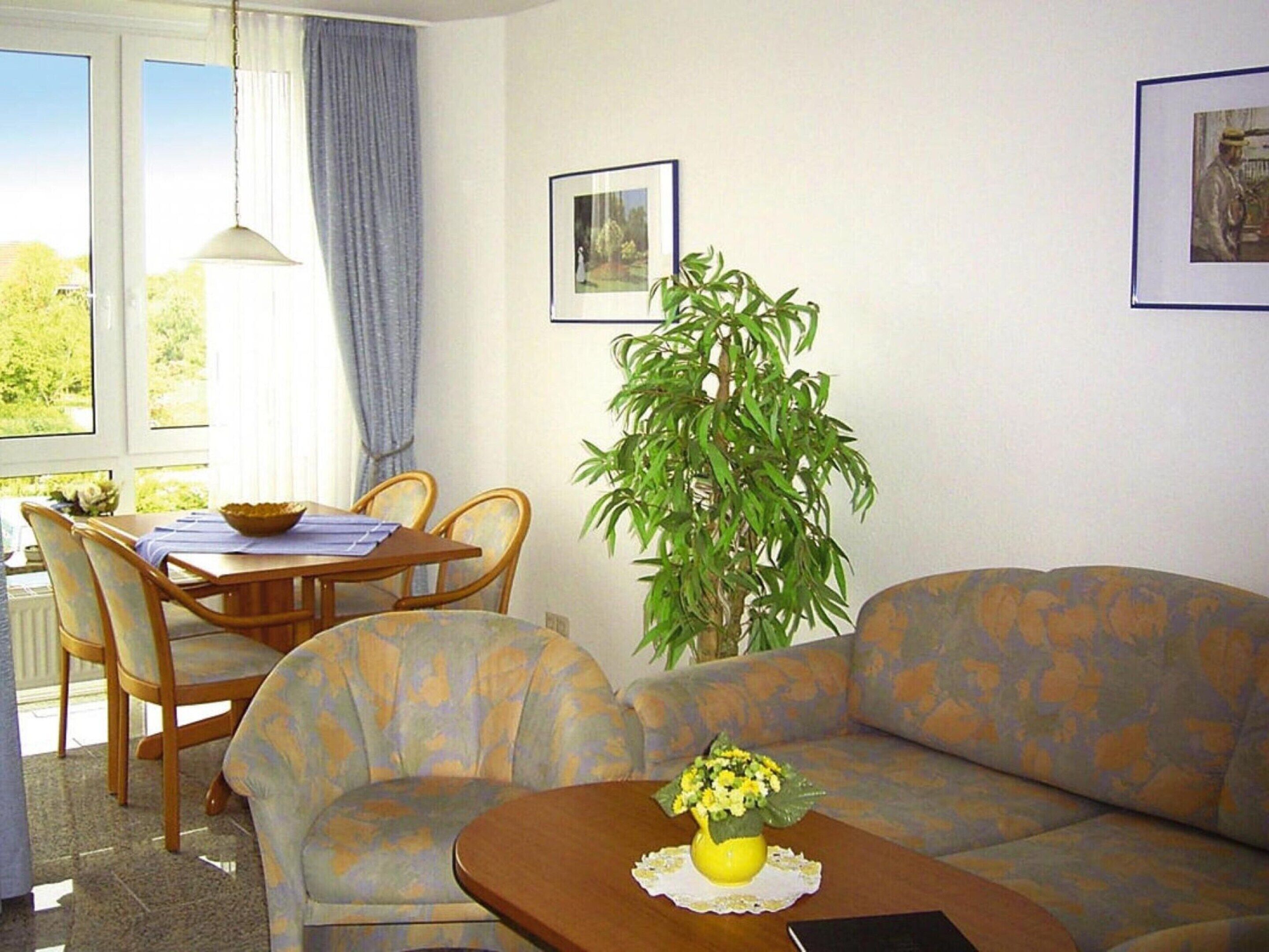 A living room with a sofa, a dining table with chairs, a potted plant, and framed pictures on the wall.
