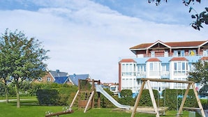 A playground with a slide and swings in a grassy area with houses in the background. - Ferienwohnung in Cuxhaven-duhnen (Cuxhaven)