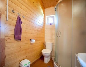Ein Badezimmer mit Holzverkleidung, das eine Toilette, eine Duschkabine und ein Handtuch an der Wand zeigt.